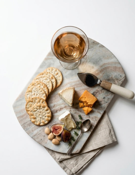 Marble platter with cheese, crackers, figs, and a glass of white wine on a light background