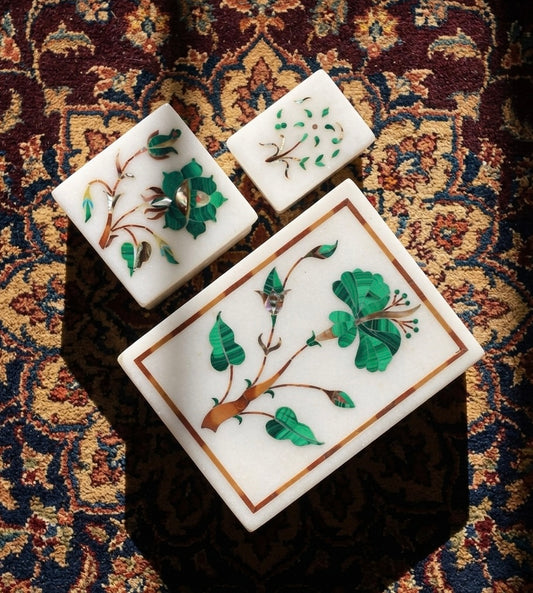 Vyasaara - Three decorative stone boxes with floral designs on a patterned fabric background