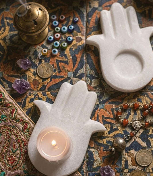 Vyasaara - Decorative items including a marble Hamsa hand, lit candle, crystals, and coins on a patterned surface.