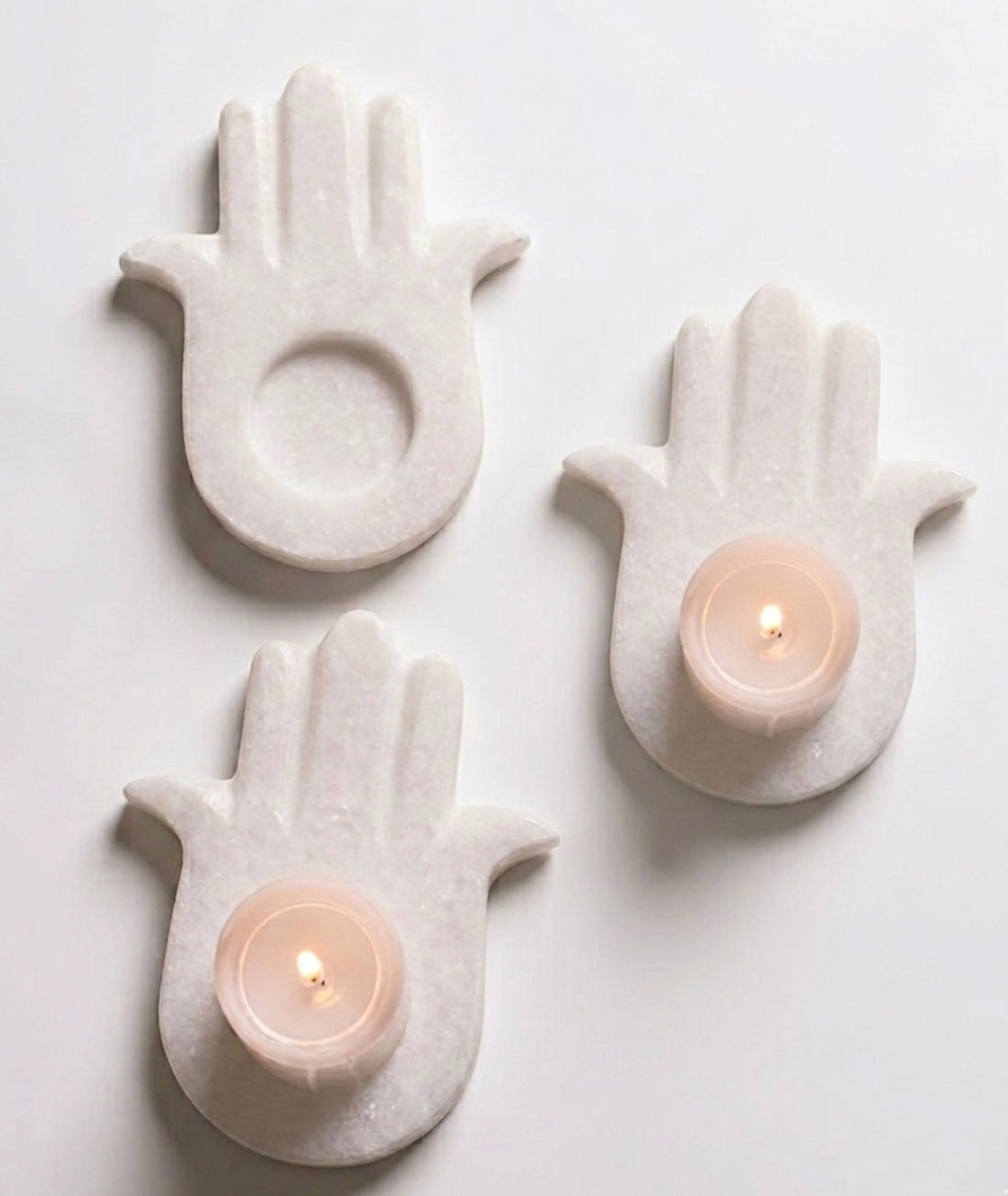 Vyasaara - Three white ceramic hand-shaped candle holders with lit candles on a light gray background