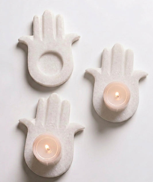 Vyasaara - Three white ceramic hand-shaped candle holders with lit candles on a light gray background