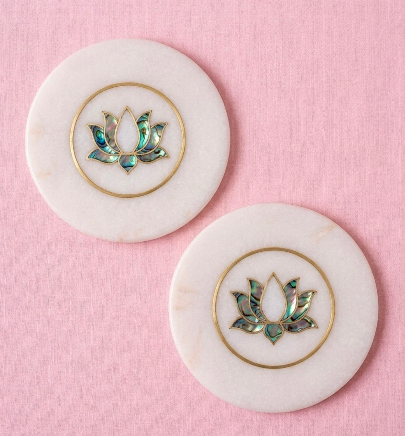 Two marble coasters with lotus flower designs on a pink background