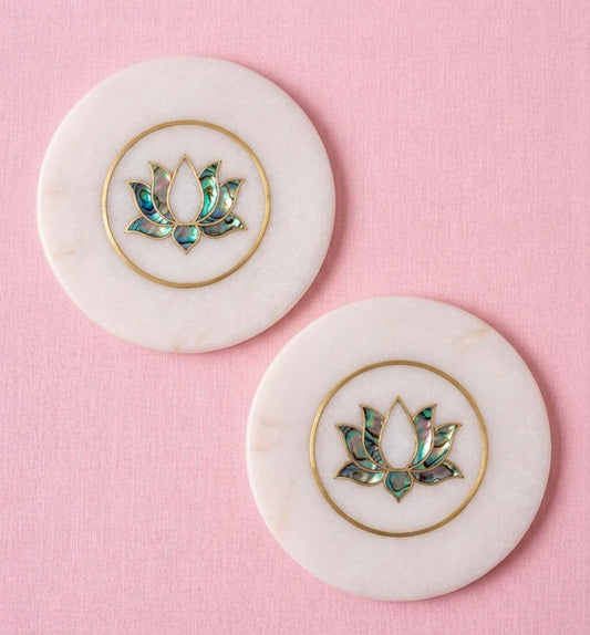 Two marble coasters with lotus flower designs on a pink background