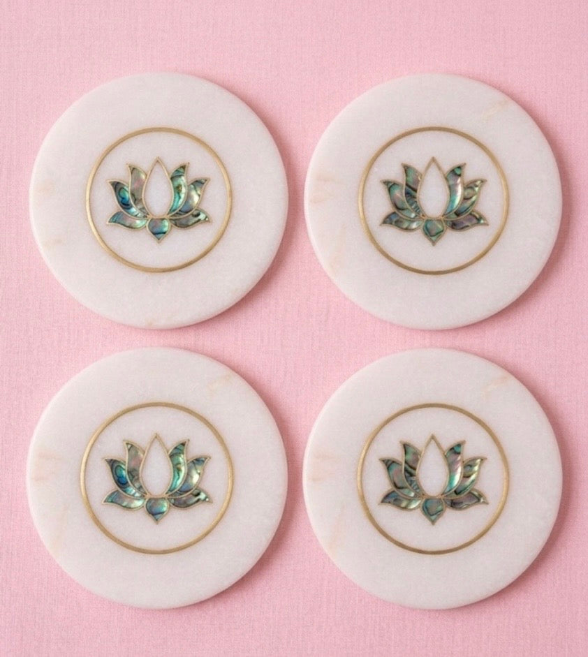 Four white circular coasters with decorative lotus patterns on a pink background