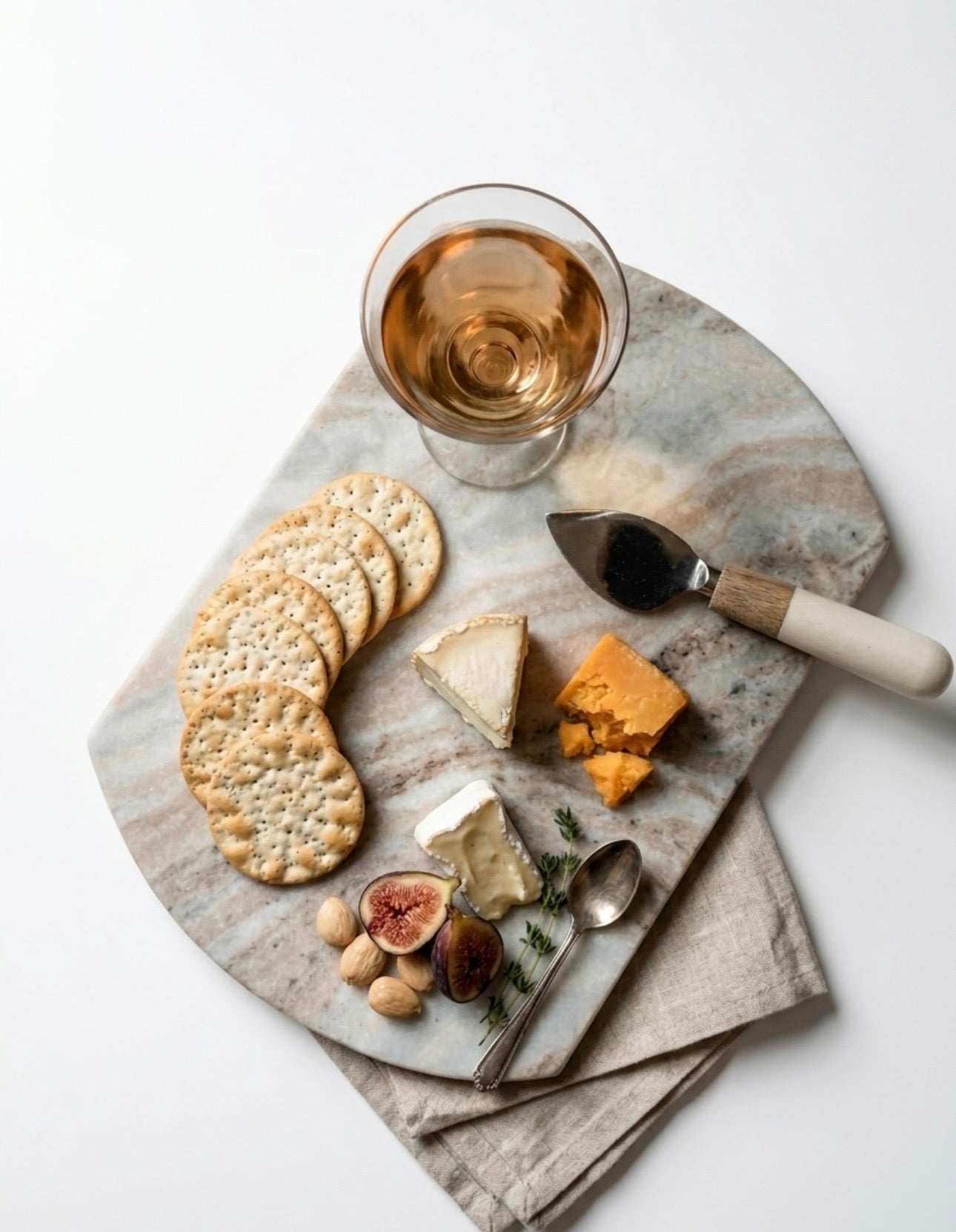 Marble platter with cheese, crackers, figs, and a glass of white wine on a light background