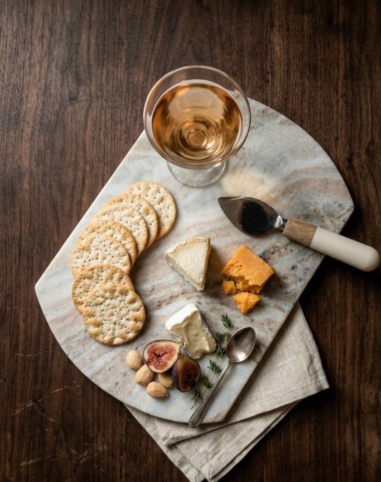 Platter with cheese, crackers, figs, and a glass of white wine on a wooden table.